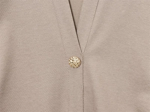 Detail des V-Ausschnitts am khakifarbenen Kleid mit strukturiertem Stoff und Goldknopf
