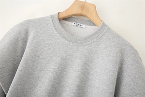 Detail eines grauen Sweatshirts mit Rundhalsausschnitt und Markenetikett am Kragen
