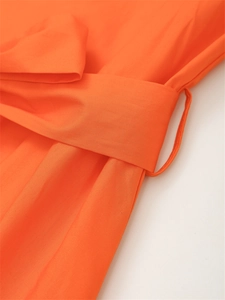 Primer plano de un vestido naranja brillante con cinturón de tela y trabillas de talle