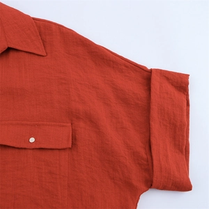 Detail eines brennend orangefarbenen Leinenhemdes mit klassischem Kragen und Metallknopf