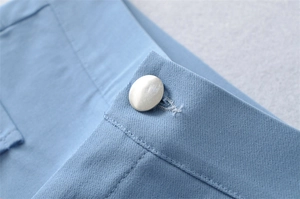 Macro detail of high-waist denim shorts featuring a silver button and clean stitching