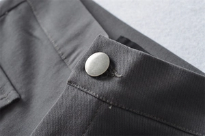 Macro shot of charcoal grey twill fabric waist detail with a matte silver metal button