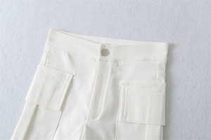 Detail of white high-waisted cargo shorts featuring utility pockets and silver metal button