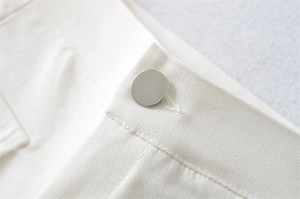 Detailed close-up of a silver metal button on white high-stretch vintage workwear shorts