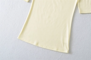 Detailed close-up of light yellow knit fabric and double-needle hem on a slim-fit shirt