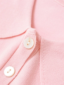 Détail du col d'un polo en tricot rose avec boutons blancs et texture fine