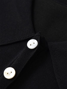 Détail du col polo en maille noire avec deux boutons nacrés et texture de tricot fine
