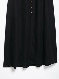 Detail view of the single-breasted front buttons and slit hem on a black linen midi dress