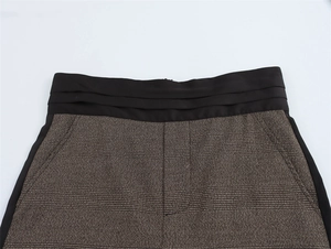 Dettaglio dei pantaloni a quadri a vita alta con cintura a pieghe nera e tasca laterale