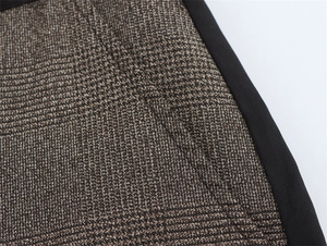 Dettaglio macro dei pantaloni a quadri con motivo pied de poule marrone e piping nero