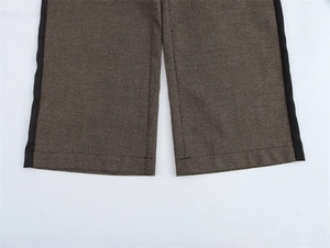 Dettaglio dei pantaloni a gamba larga a quadri marroni con strisce laterali nere