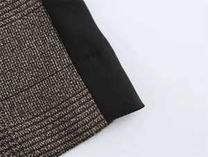 Dettaglio del tessuto a quadri marrone e delle cuciture nere dei pantaloni a vita alta