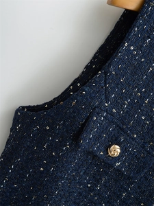 Detailansicht von marineblauem Tweed mit goldenen Pailletten und geprägtem Metallknopf