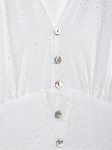Dettaglio del ricamo floreale traforato bianco e bottoni perlati su un abito con scollo a V