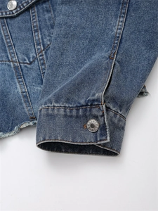 Detail einer blauen Jeansjacke mit ausgefranstem Saum, Kontrastnähten und Metallknöpfen