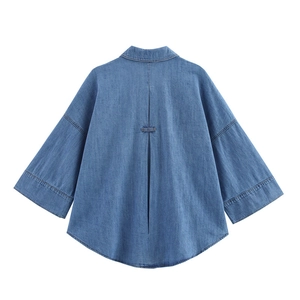 Detail view showing back pleat and loose silhouette of light blue denim shirt with curved hem