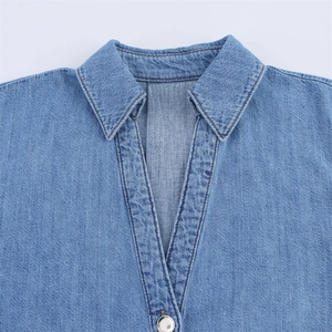 Detail of light blue denim shirt showing turn-down collar and silver metal button