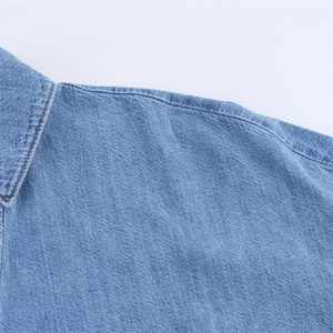 Close-up of light blue denim fabric texture and stitching detail on the shirt collar