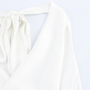Detail des weißen Satin-Halterneck-Tops mit seidiger Textur und elegantem Bindedetail