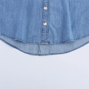 Detailed close-up of light blue denim shirt hem with polished metal buttons and stitching