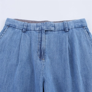 Detail view of light blue denim trousers featuring waist pleats and front pockets