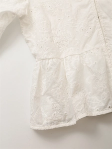 Dettaglio della camicia in cotone bianco con ricamo floreale e bordo a volant