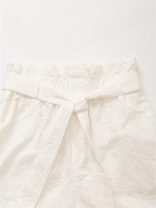Dettaglio ravvicinato di pantaloncini bianchi a vita paperbag con ricamo floreale traforato