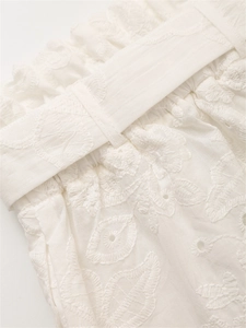 Dettaglio di pantaloncini bianchi in cotone con ricami floreali e vita elastica arricciata