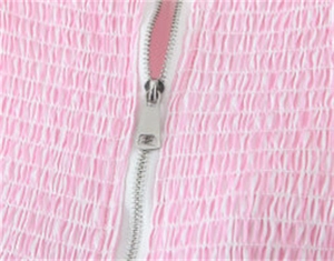 Makroaufnahme von Silber-Metallreißverschluss und rosa gesmokter Stofftextur am Sommeroutfit