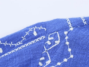 Makroaufnahme weißer Stickerei auf strukturiertem blauem Stoff mit präziser Nahtarbeit