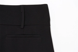 Close-up of black wide-leg trousers showing the waistband, belt loop and welt pocket