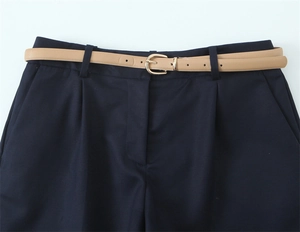 Dettaglio dei pantaloncini blu navy a pieghe con cintura sottile e fibbia dorata