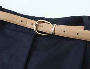 Dettaglio di pantaloncini blu scuro con una sottile cintura cammello e fibbia dorata a ferro