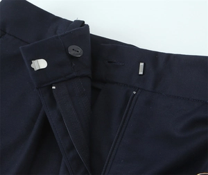 Dettaglio dei pantaloncini blu scuro con bottone, gancio metallico e chiusura a zip