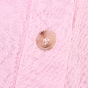 Détail du tissu de chemise en lin rose montrant la texture et un bouton marron