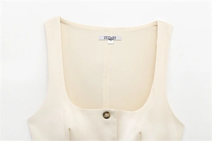 Detail of minimalist cream-colored buttoned top with square neckline and resin button