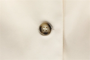 Detailed macro shot of a brown marble button on a beige minimalist woven garment