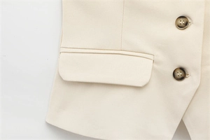 Close-up of cream blazer with fine stitching on flap pocket and dark tortoiseshell buttons