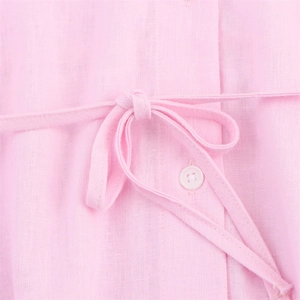 Détail macro du tissu en lin rose d'une chemise avec nœud et bouton rond blanc