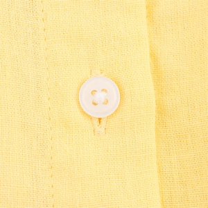 Détail macro d'une chemise en lin jaune pâle montrant la texture et un bouton blanc