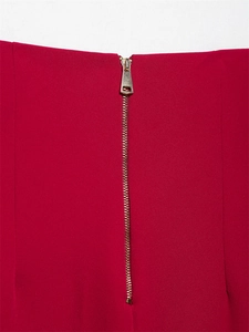 Dettaglio dei pantaloni rossi con cerniera in metallo dorato lucido e cursore moderno