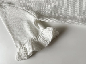 Détail d'un pull en maille blanche avec texture côtelée et poignets à volants élégants
