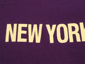 Detail of purple knit fabric with yellow New York lettering in a retro varsity style