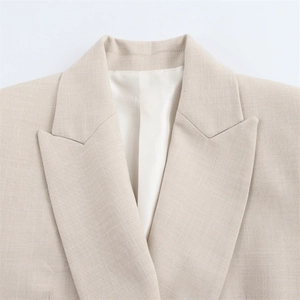 Detailaufnahme des steigenden Revers eines beigen Blazers mit feiner Textur und weißem Futter