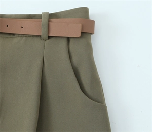 Dettaglio dei pantaloni verde militare a vita alta con cintura marrone e rifiniture a pieghe