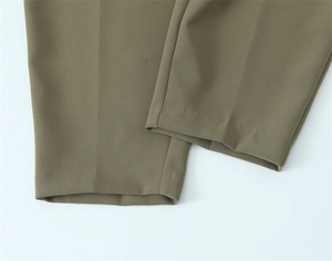 Dettaglio macro dei pantaloni a gamba dritta che mostra il tessuto verde oliva e l'orlo