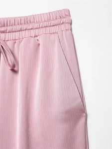 Detail van een roze satijnen broek met elastische taille, trekkoord en zijzak