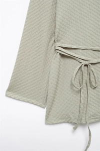 Detail view of sage green textured V-neck top showing soft waffle fabric and waist tie