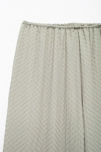 Detail of light grey-green trousers featuring elastic smocked waist and pleated texture fabric