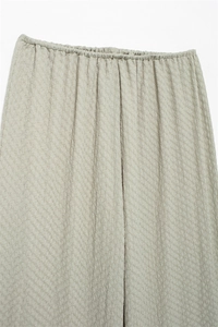 Detailed view of elastic waistband and textured light sage green fabric on casual trousers